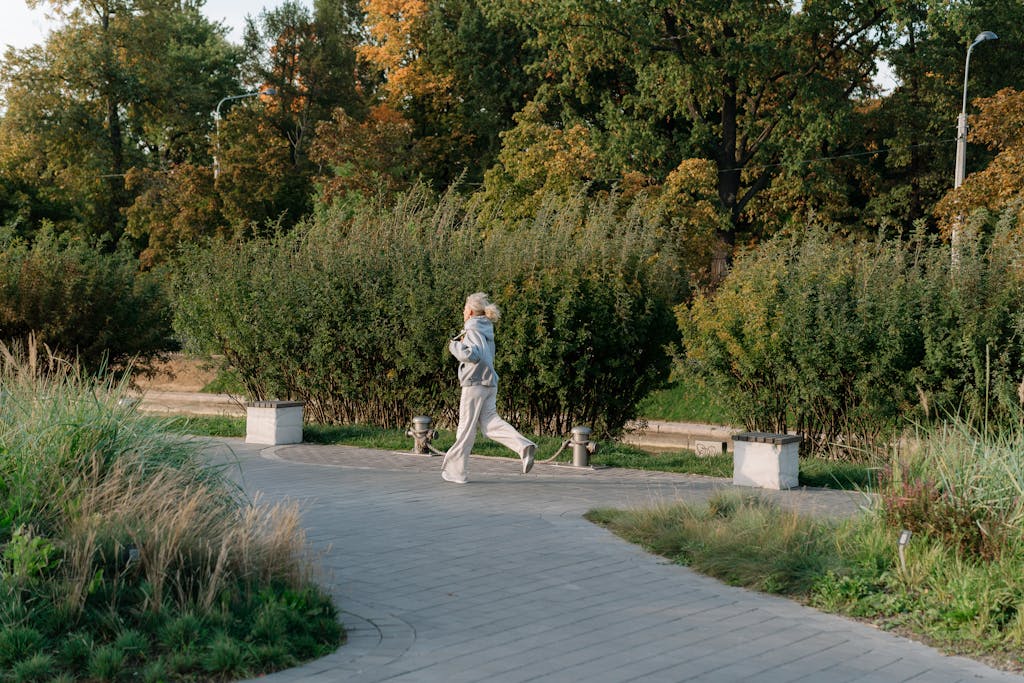 Elderly woman staying active by jogging in a scenic park surrounded by lush greenery.