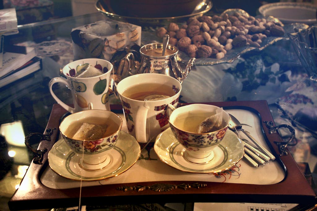 A warm setting with porcelain cups of tea on a tray, surrounded by nuts and elegant dishware.