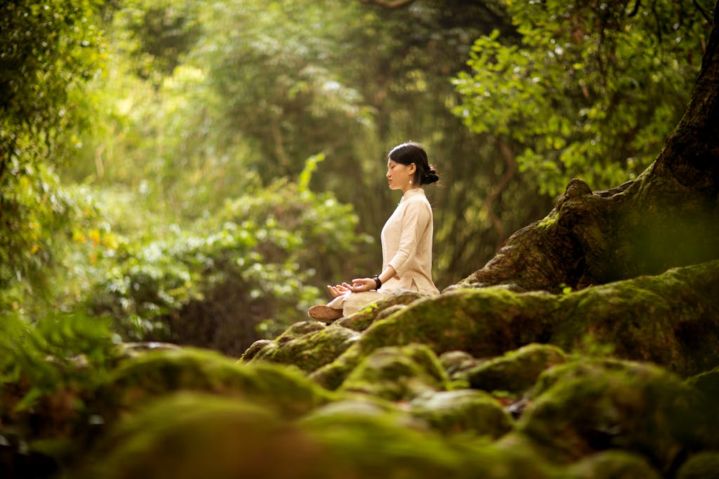 A woman in serene meditation in a lush forest, surrounded by trees and moss.