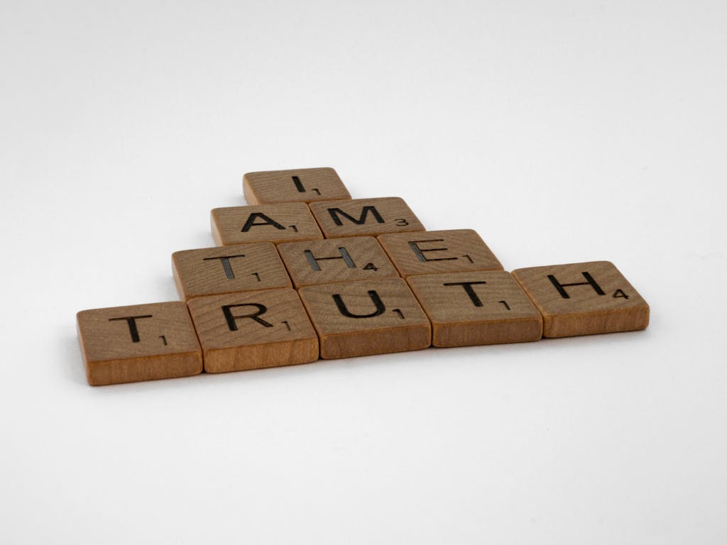 Close-up of wooden Scrabble tiles on a white background spelling 'I Am The Truth'.